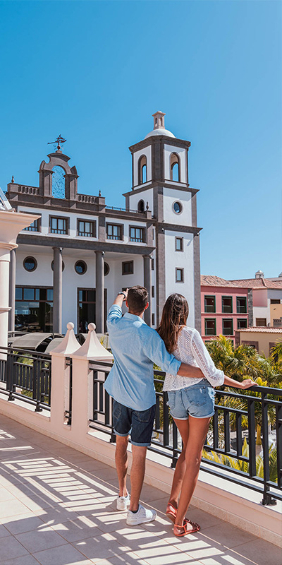  Imagen icónica de pareja de clientes frente a la fachada del hotel Lopesan, Resort & Thalasso en Meloneras, Gran Canaria 